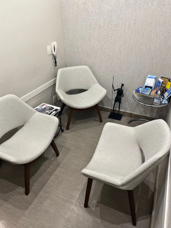 Fotografia de sala de espera de consultório odontológico com três cadeiras brancas e um quadro abstrato.